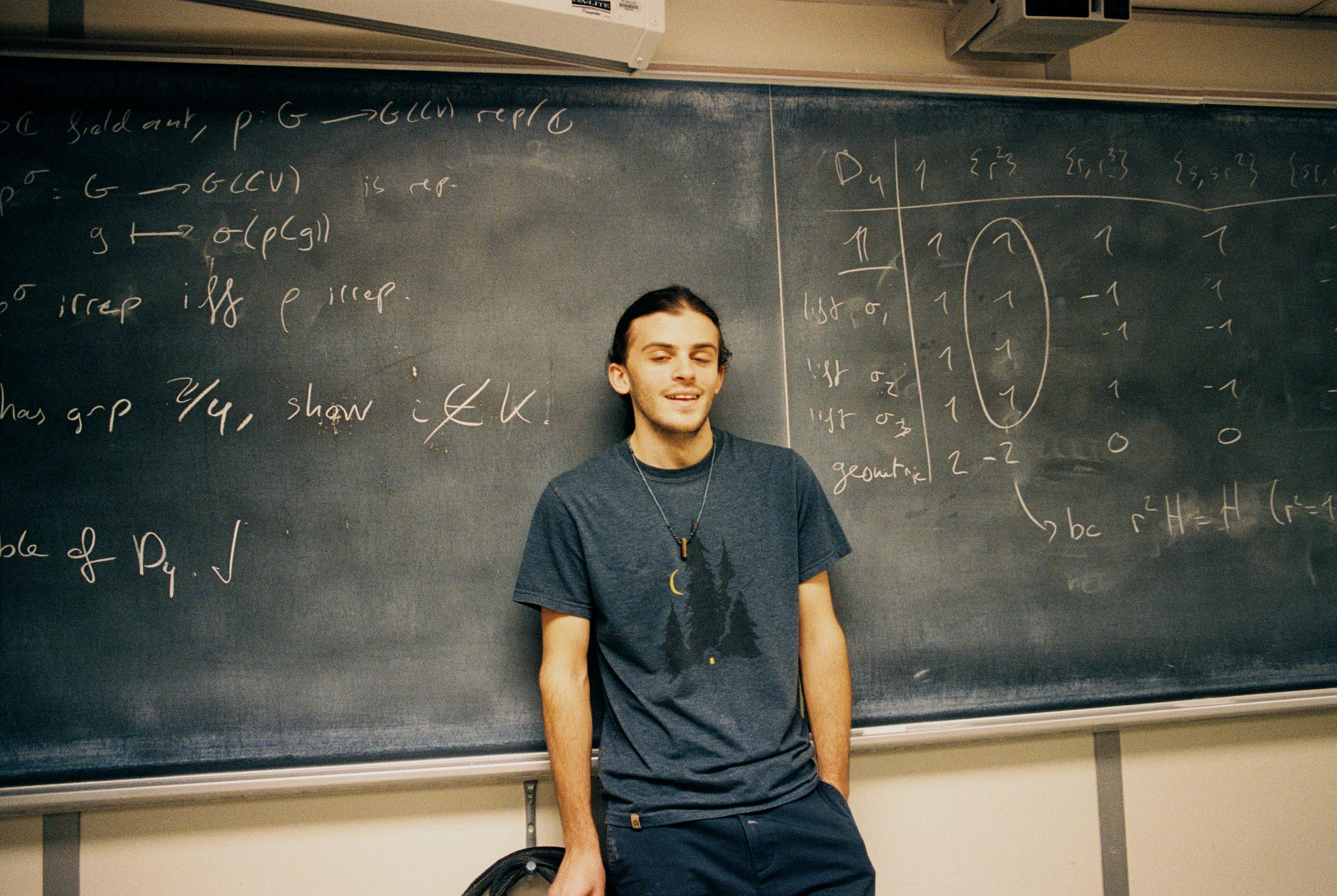 Young man standing infront of chalk board; chalk board detail representation theory